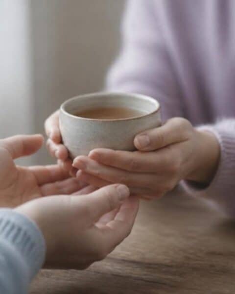 Manos que ofrecen una taza de té a otras manos sobre una mesa de madera
